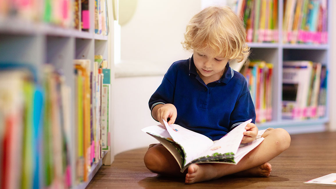 Junge sitzt mit Buch auf dem Boden