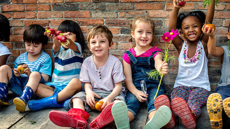 Kindergartenkinder sitzen an einer Mauer